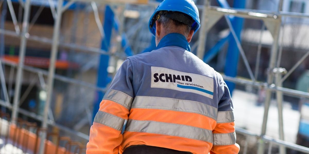 Schmid Bauarbeiter trägt Schmid Arbeitsjacke und blauer Helm auf Baustelle.