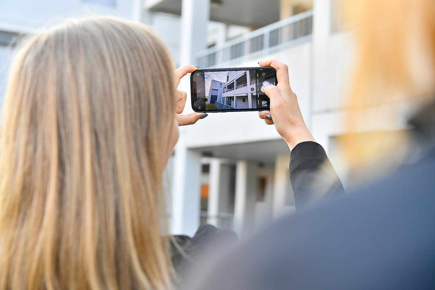 Schmid Projektleiterin fotografiert mit dem Handy die Liegenschaft von aussen.