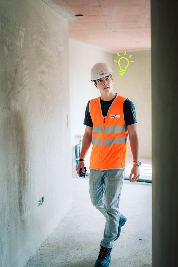 Schmid Lernender Zeichner trägt Helm und Leuchtveste auf der Baustelle.