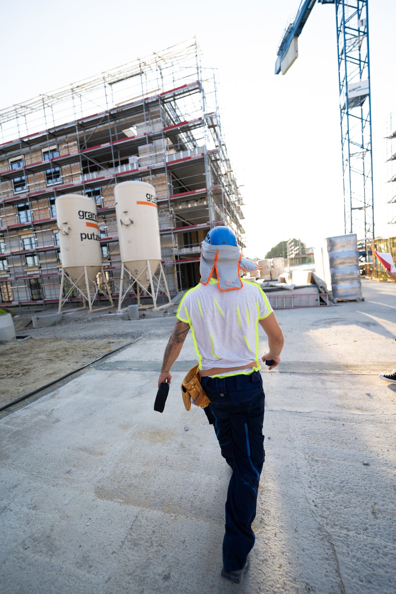 Schmid Lernener Fassadenbauer von Rückseite fotografiert trägt weisses T-Shirt und Helm mit Sonnenschutz.