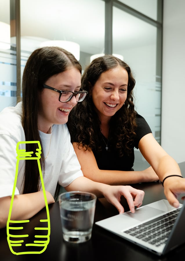 Zwei Schmid KV Lernende schauen gemeinsam lächelnd in den Laptop Bildschirm.