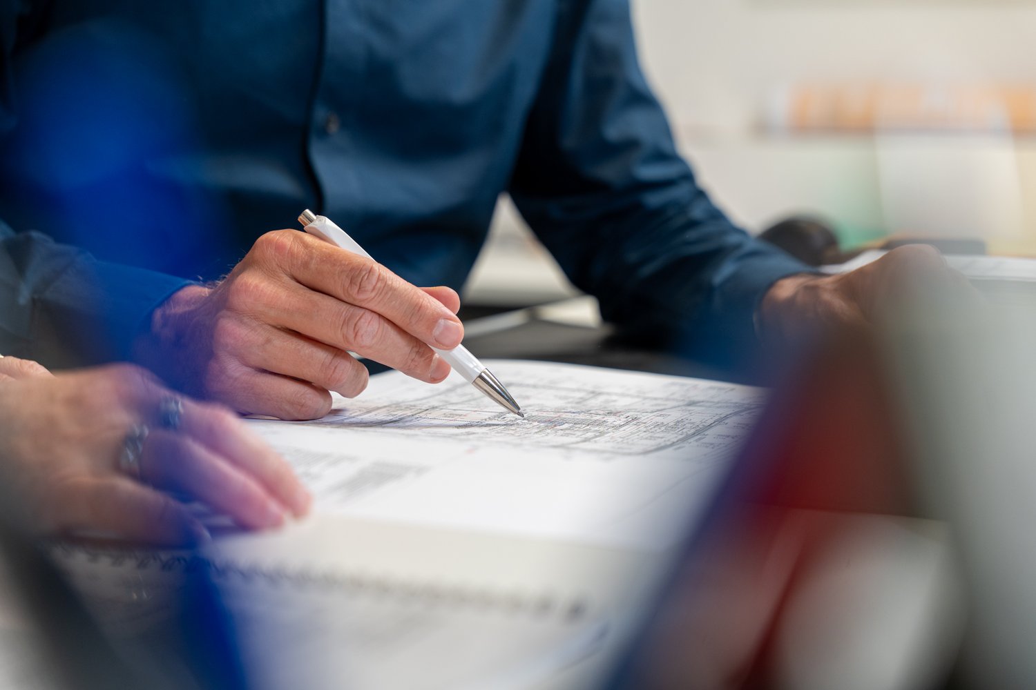 Hände die auf einem Plan liegen. Eine Hand hält einen Stift