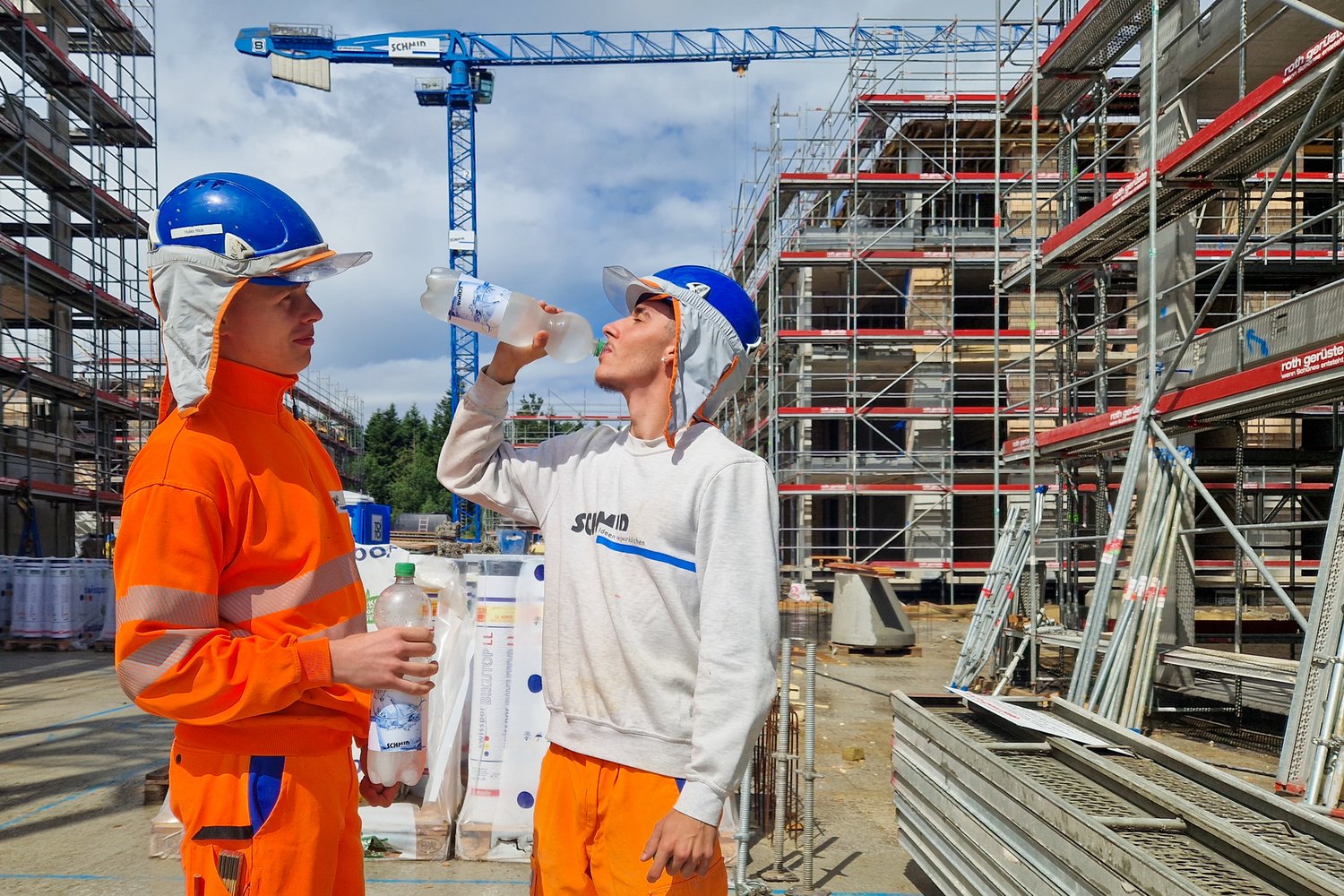 Lernende auf der Baustelle und trinken Mineralwasser und tragen den Sonnenschutz