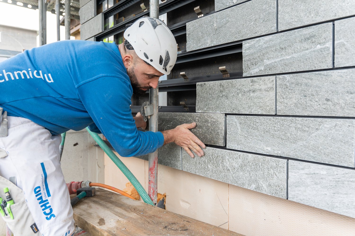 Mitarbeiter bringt eine Steinplatte an die Fassade an