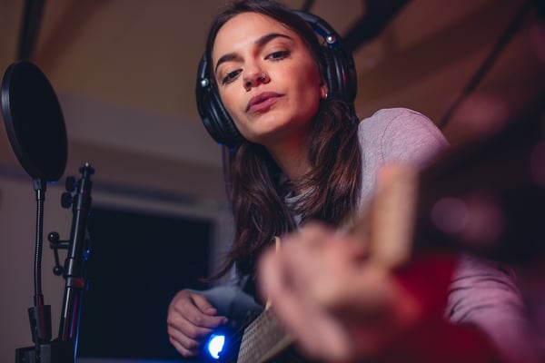 Musikerin mit Kopfhörer die Gitarre spielt.